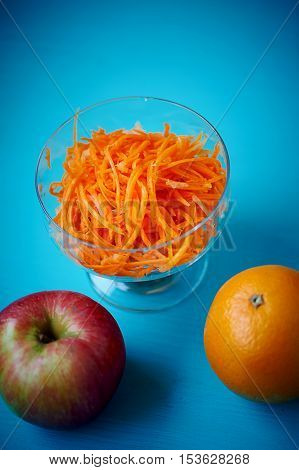 Grated carrot in a glass Cremant, on a blue background with an Apple and orange
