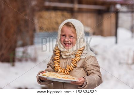 Sweet girl in old Russian scarf on the head with lengths in a plate and bread-rings around the neck walking down the street