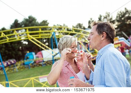 Senior couple having a good time at the fun fair, blowing soap bubbles with bubble wand.
