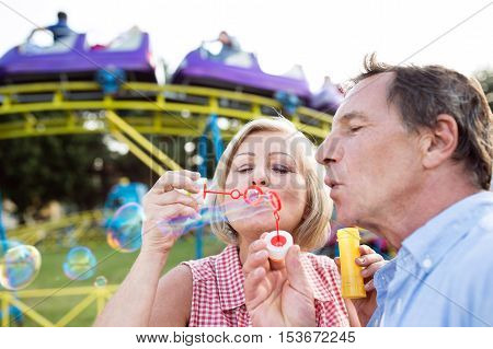 Senior couple having a good time at the fun fair, blowing soap bubbles with bubble wand.