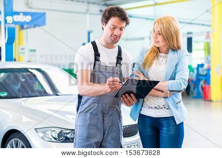 Male workshop mechanic handover car with checklist to client 