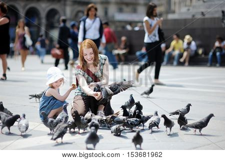 Young mother and daughter feeding pingeons on summer day