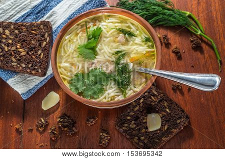 Chicken soup with pasta and vegetables in a clay bowl on wooden table top view