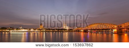 Illuminated Cologne Cathedral and bridge at night in Cologne, panoramic view