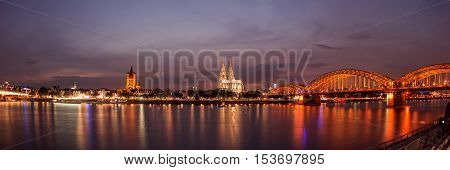 Illuminated Cologne Cathedral and bridge at night in Cologne, panoramic view