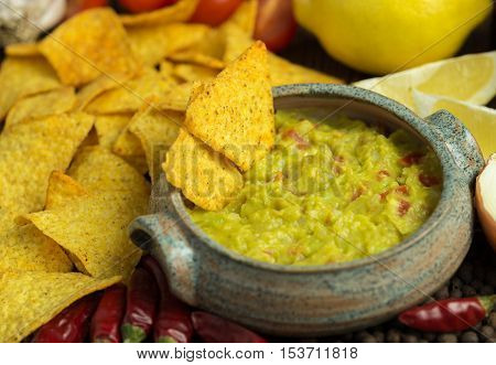 Guacamole in home crafted bowl with tortilla chips and chilli around.