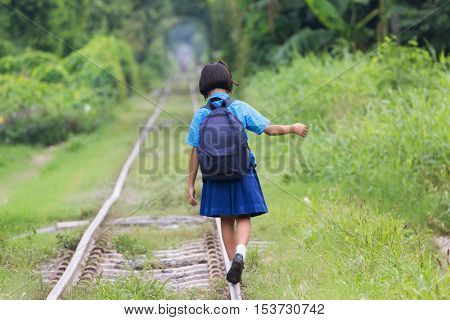 Thai schoolgirl in traditional costume walking and balancing on the railway of the Talat Phlu district in Bangkok.