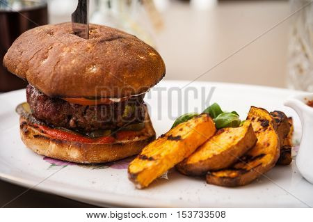 Beefburger with fried sweet potatoes served on a white plate