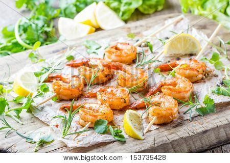 Seafood. Shelfish. Grilled fried Shrimps Prawns on wooden skewers with spices and fresh herbs on wooden rustic cutting table on wooden background. Srimps prawns brochette kebab. Barbecue srimp