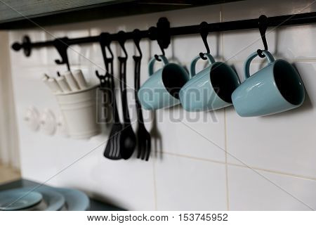 blue cups is located on the pure white wall in the kitchen above the owen. closed to cups are located some other applience needed for cooking