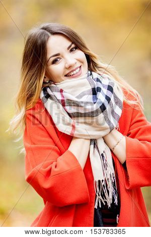 Beautiful young girl in red autumn coat and scarf on the shoulders happily smiles autumn day in nature