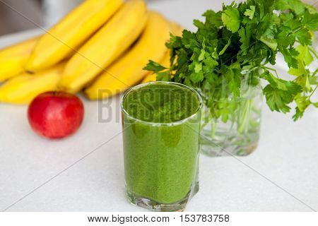 healthy food, organic food and diet concept - closeup of fresh green juice in a glass with parsley and a banana on a kitchen table