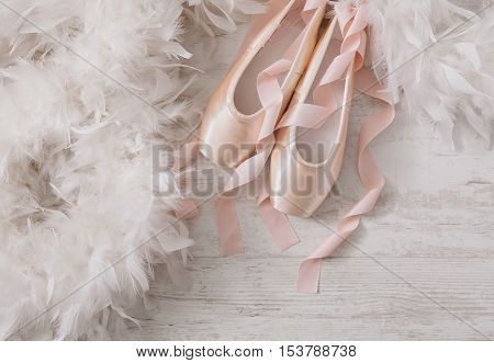 Pastel pink ballet shoes background. New pointe shoes with satin ribbon lay on white rustic shubby chic wood near feather boa, top view with copy space