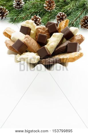 A large variety of Aachener Printen (German gingerbread speciality) and Dominosteine arranged on a white porcelain plate with fir tree twigs and pine cones on white background.