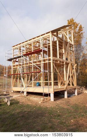 Metal scaffolding around the unfinished house. Construction of ecological house. Wooden frame of house under construction.Framed New Construction of a House. Timber house in building process