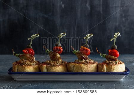 Spanish tapas. Montaditos. Bread slices with tuna, peppers and capers. Typical appetizer. Dark photo