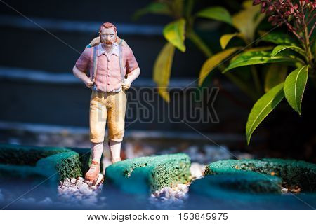 Small hiker figure walking with backback in garden.