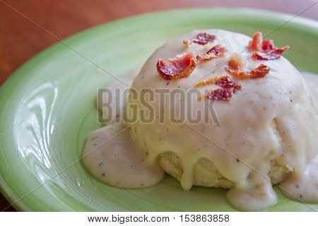 Biscuits and Gravy topped with bacon on a green plate