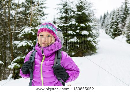 Woman hiking in white winter forest woods with backpack. Young girl walking on snowy trail. Recreation fitness and healthy lifestyle camping outdoors. Motivation and inspirational winter landscape.