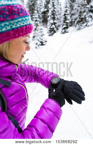 Woman hiker checking the elevation on sports watch smartwatch with altimeter app in winter woods and mountains. Girl trekker in white snowy forest trekking with electronics equipment technology.