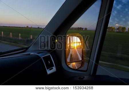 Side rear-view mirror in the evening on the road during sunset