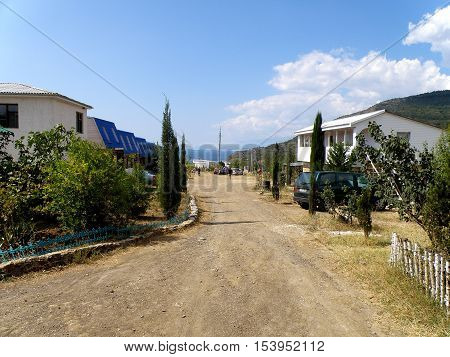 Dirt road passes by the house on a clear sunny day.