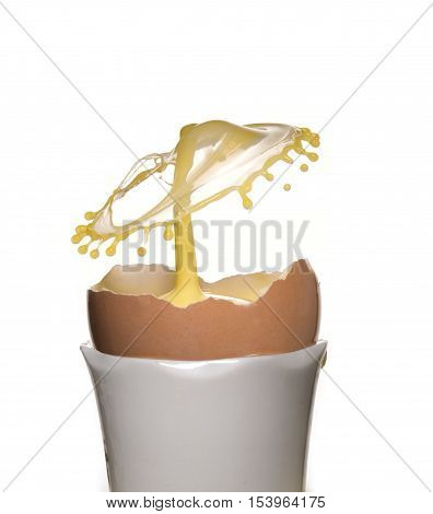 Part eggshell in white eggcup with yellow coloured water drop collision.