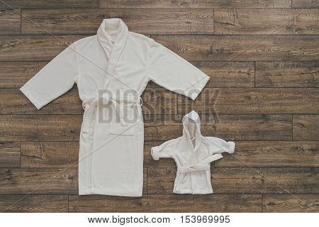 Two white bathrobes for mom and baby. Holding hands. wooden background