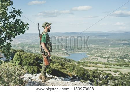 Hunter young man standing on peak mountain during hunting period - Bearded guy waiting for the pray with wonderful panoramic view background - Hunting concept - Soft desaturated warm vintage filter