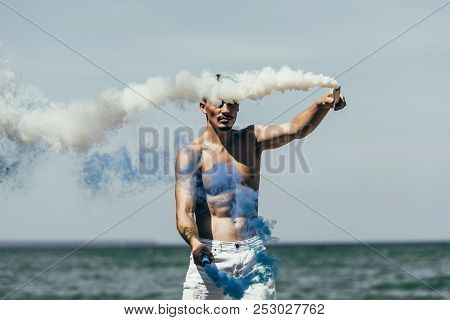 Attractive Man Holding Blue And White Smoke Sticks In Front Of Sea