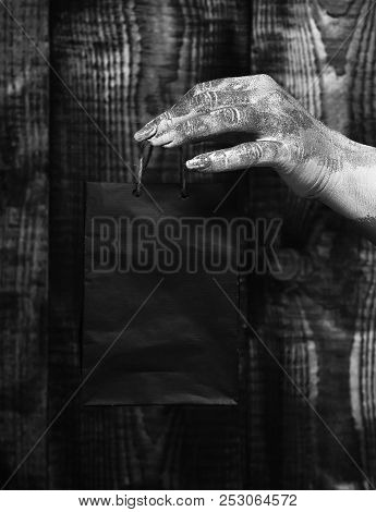 Female Hand Smeared In Golden Paint Or Glister Holding Black Selective Focus Package Or Bag On Brown