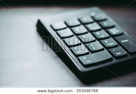 A Black Plastic Numeral Keypad Is Placed On The Wooden Table Focused On The Bottom Half Side With Li