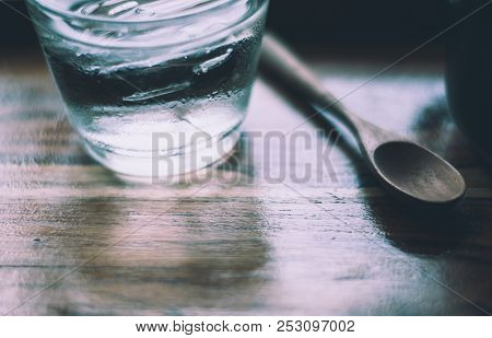 A Glass Of Cold Water With Few Ice Inside Placed Together With Wooden Spoon, All Of Them Is In Woode