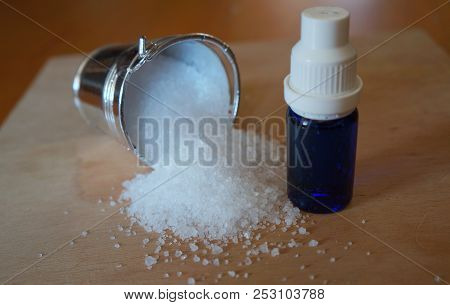 Natural Salt In Silvery Bucket And Blue Etherial Oil Bottle On Weathered Wooden Table