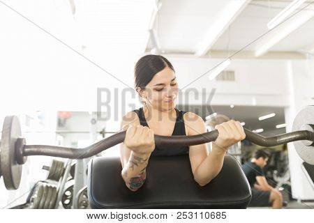 Determined Woman Working Out With Curl Bar While Sitting On Exercise Machine In Gym