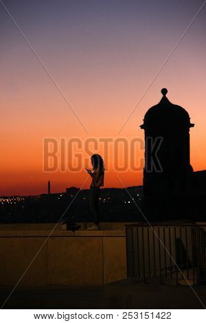 Young Woman Surf Mobile Phone On Background Of Glowing Orange Sunset