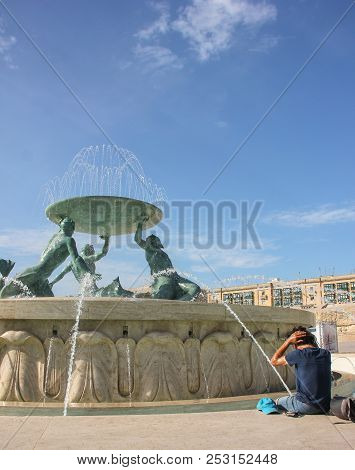 Young Man Sit On Neptune Fountain In Hot Summer Day Near Valletta Main Entrance