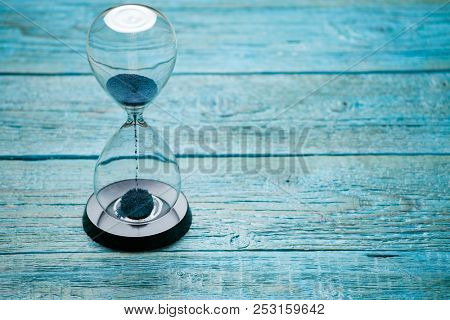 Photo of hourglass with blue sand on wooden background,