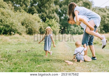 Family With Children Spending Time On Summer Feild, Father Piggybacking Mom