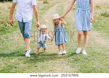 Family With Two Kids Holding Hands And Walking On Summer Feild
