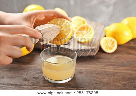 Young Woman Squeezing Lemon Juice With Reamer Into Glass On Table