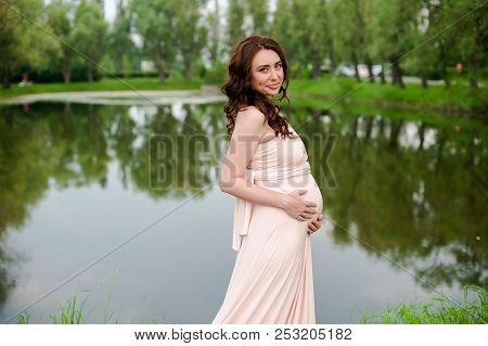 Smiling Pregnant Woman 25-29 Year Old Resting By The Lake. Posing Outdoors. Motherhood. Maternity
