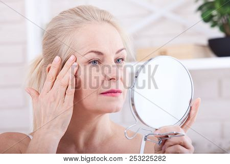 Forty Years Old Woman Looking At Wrinkles In Mirror. Plastic Surgery And Collagen Injections. Makeup