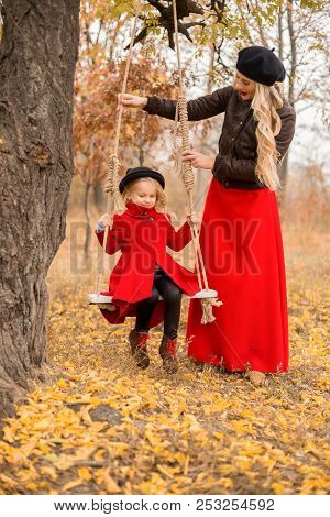 Beautiful Mother In A Long Dress Is Swinging On A Hinged Swing Little Daughter In A Red Coat In An A