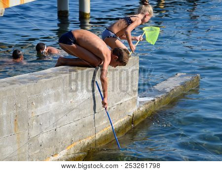 Novorossiysk, Russia - August 06, 2018: Children Catch A Net Of Small Fishes In Sea Water.