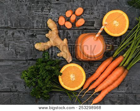 Freshly Made Carrot Smoothie, Bunch Of Carrots, Parsley, Orange And Ginger Root On A Rustic Table. T