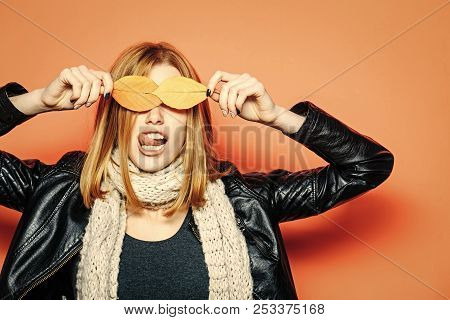 Woman With Autumn Leaves As Glasses In Leather Jacket And Scarf On Orange Background Show Tongue