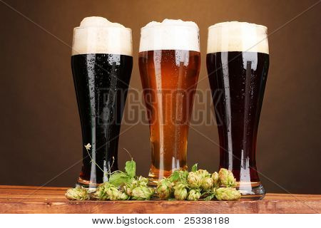 tre bicchieri con birre diverse e hop sul tavolo di legno su sfondo marrone