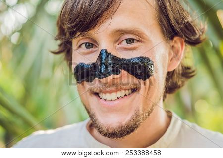 Happy Man With Black Mask On The Face. Photo Of Man Receiving Spa Treatments. Beauty Skin Care Conce
