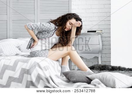 Brunette Girl Female Woman With Curly Hair And Grey Pajamas Sleepwear With Hearts Sitting On The Bed